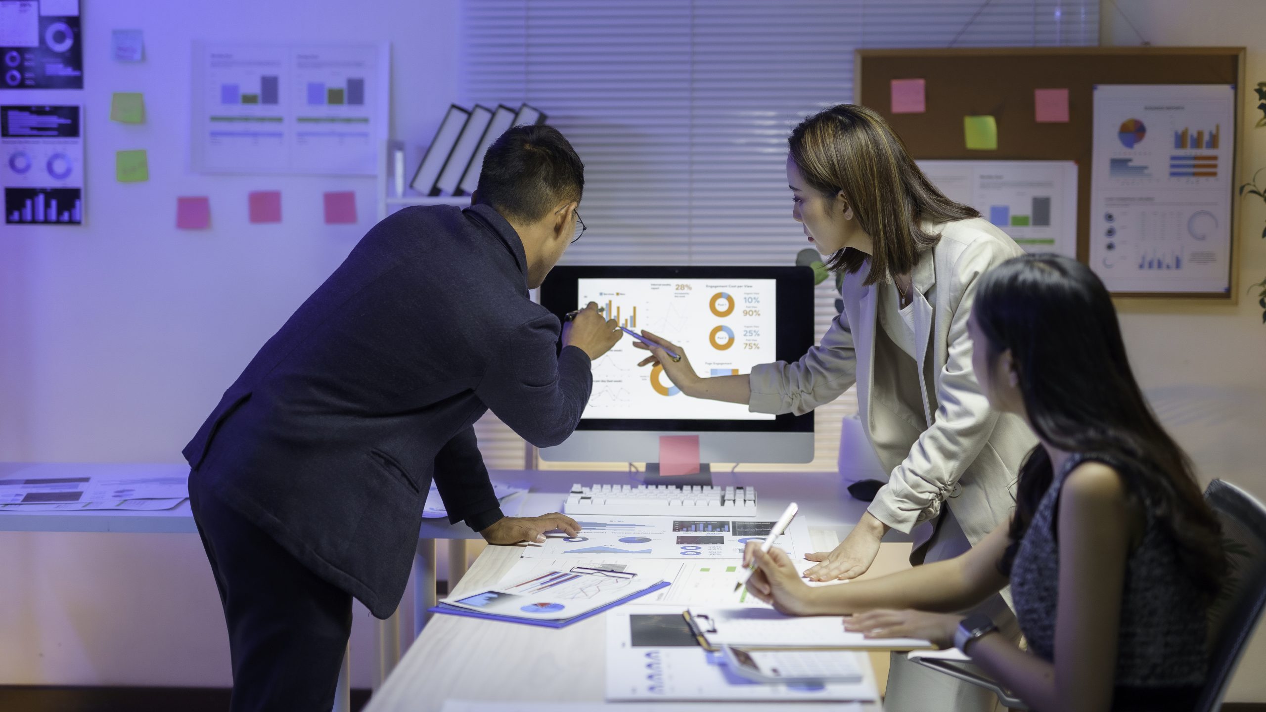 Asian businesspeople analyzing financial charts on computer screen in office meeting